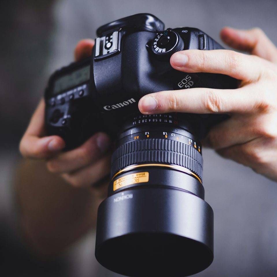Jemand hält eine Canon Kamera mit einem großen Objektiv in den Händen.